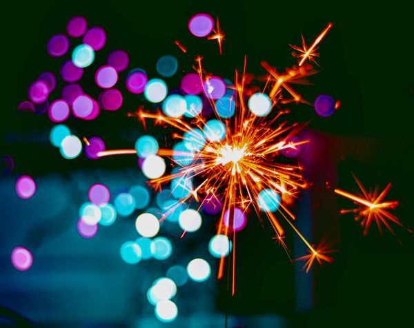 Lit sparkler in front of blurred purple and blue lights.